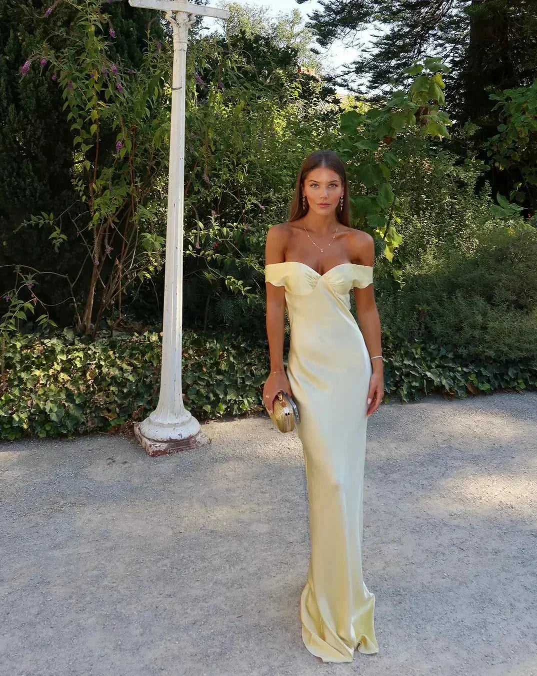 Off-shoulder yellow maxi dress made from lightweight fabric, featuring a flowing silhouette and a matching clutch for style.