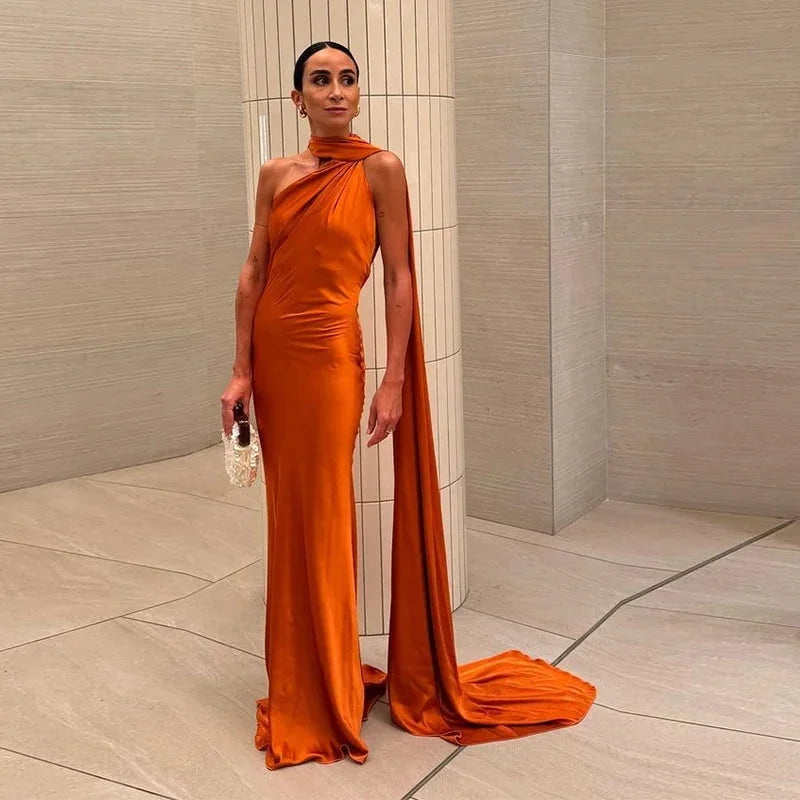 Orange satin floor-length cape dress with halter neck design, featuring a flowing silhouette and smooth, elegant fabric.