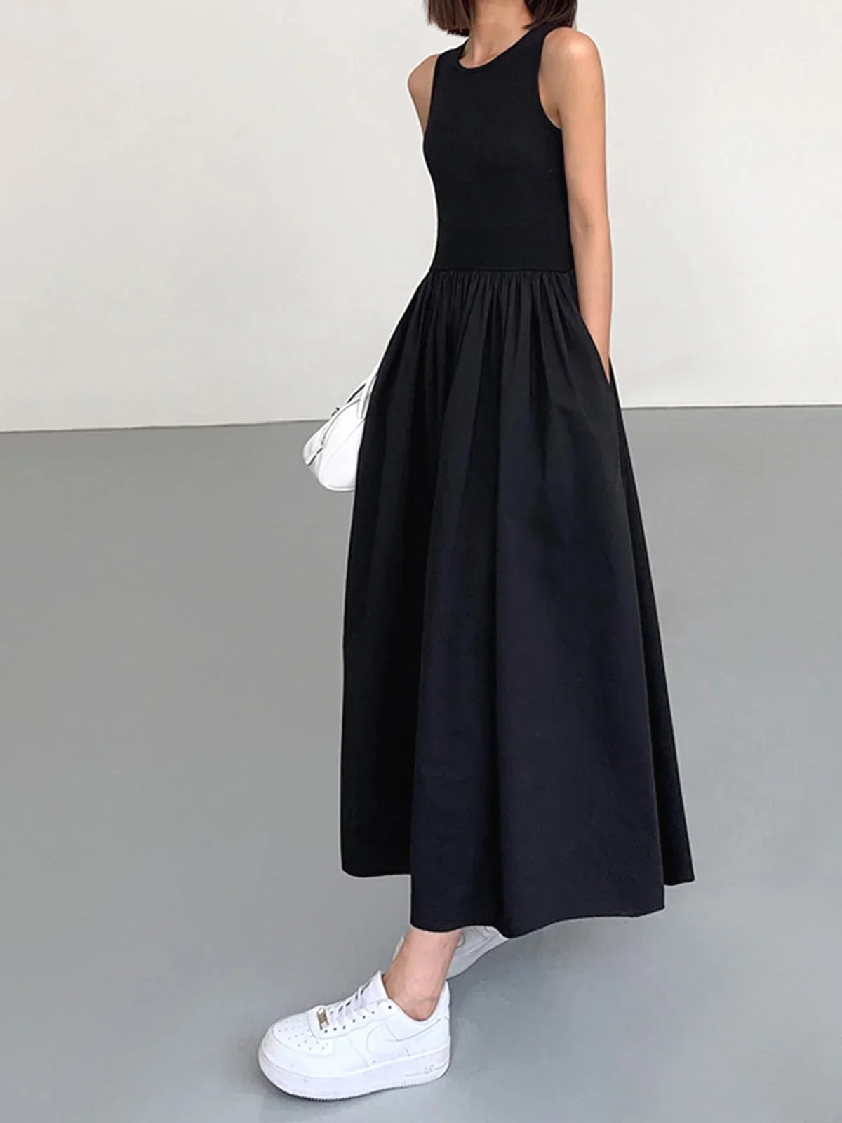Black sleeveless jersey midi dress featuring a flowing skirt, designed for comfort and ease of movement. Perfect for warm…