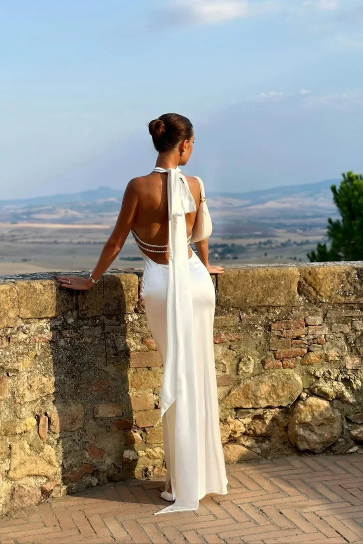 Women’s white backless maxi dress made from soft fabric, featuring pearl accents and a stylish bow detail at the waist.